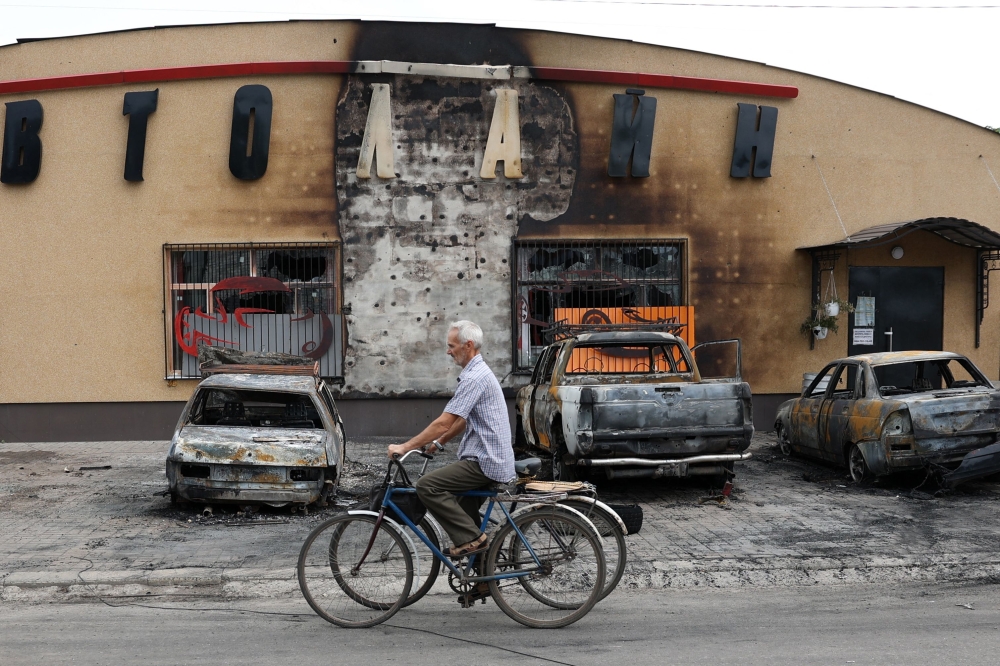 An elderly man riding a bicycle pushes the bike of his wife killed by a cluster bomb in Lyman, Donetsk region, on July 8, 2023. (Photo by STRINGER / AFP)
