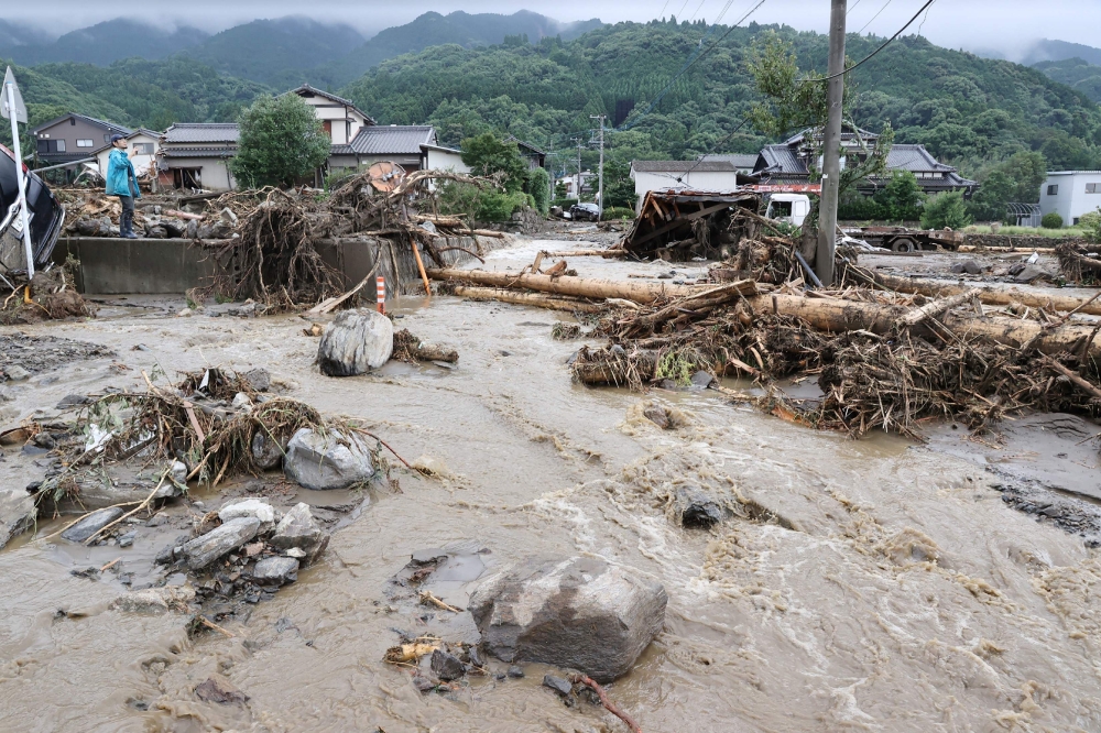 A man (L) looks at debris from flooding in the road in Tanushimarumachi in the city of Kurume, Fukuoka prefecture, on July 10, 2023, after heavy rains hit wide areas of Kyushu island. Photo by JIJI Press / AFP