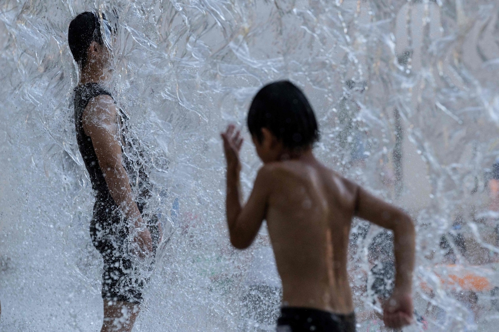 A man (L) cools off in a public water playground at a park in eastern Tokyo on July 16, 2023. (Photo by Richard A. Brooks / AFP)