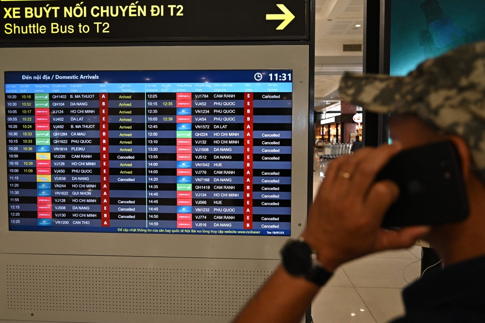 A man uses his mobile phone as a flight information board displays flights cancelled due to typhoon Talim at Noi Bai international airport in Hanoi on July 18, 2023. Photo by Nhac NGUYEN / AFP