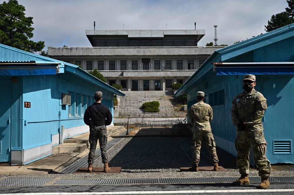 UNC (United Nations Command) soldiers (R) and a South Korean soldier (L) stand guard before North Korea's Panmon Hall (rear C) and the military demarcation line separating North and South Korea, at Panmunjom, in the Joint Security Area (JSA) of the Demilitarized Zone (DMZ) on October 4, 2022.
