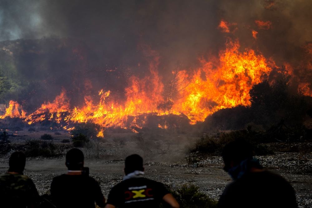 Locals watch the wildfires near the village of Vati, just north of the coastal town Gennadi, in the southern part of the Greek island of Rhodes on July 25, 2023. (Photo by Angelos Tzortzinis / AFP)