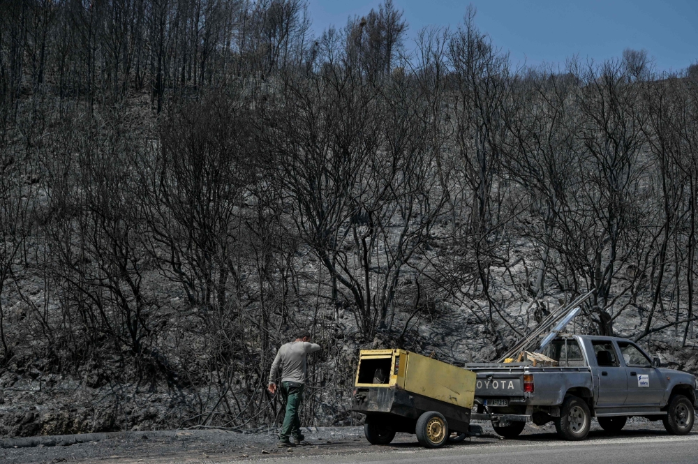 A worker walks past a burned area after a fire near Kassiopi on July 26, 2023.  (Photo by Armend NIMANI / AFP)