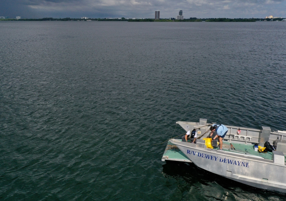 :MIAMI, FLORIDA - AUGUST 03: In an aerial view, (L-R) Nick Evans and Bradley Schonhoff conduct routine maintenance on a research buoy in Biscayne Bay on August 03, 2023 in Miami, Florida. (Photo by JOE RAEDLE / GETTY IMAGES NORTH AMERICA / Getty Images via AFP)
