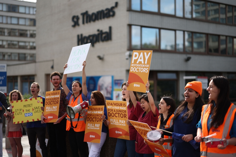 People hold British Medical Association (BMA) branded placards calling for better pay, as they stand on a picket line outside St Thomas' Hospital in central London on August 11, 2023. (Photo by Henry Nicholls / AFP)