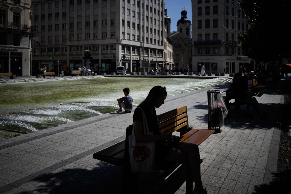 A woman sits in the shade of a tree to protect herself from the sun during a heatwave in Lyon on August 15, 2023. Photo by JEFF PACHOUD / AFP