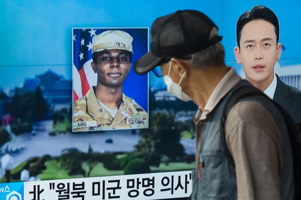 :In this photo taken in Seoul on August 16, 2023, a man walks past a television showing a news broadcast featuring a photo of US soldier Travis King (C), who ran across the border into North Korea while part of a tour group visiting the Demilitarized Zone on South Korea's border on July 18. (Photo by Anthony WALLACE / AFP)
