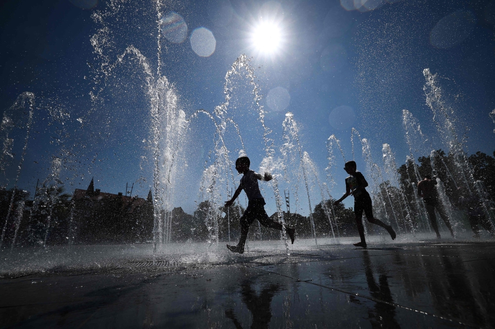 Children cool off as they run through a public fountain in Colmar, eastern France, on August 21, 2023, as France experiences a late summer heatwave. (Photo by Sebastien Bozon / AFP)