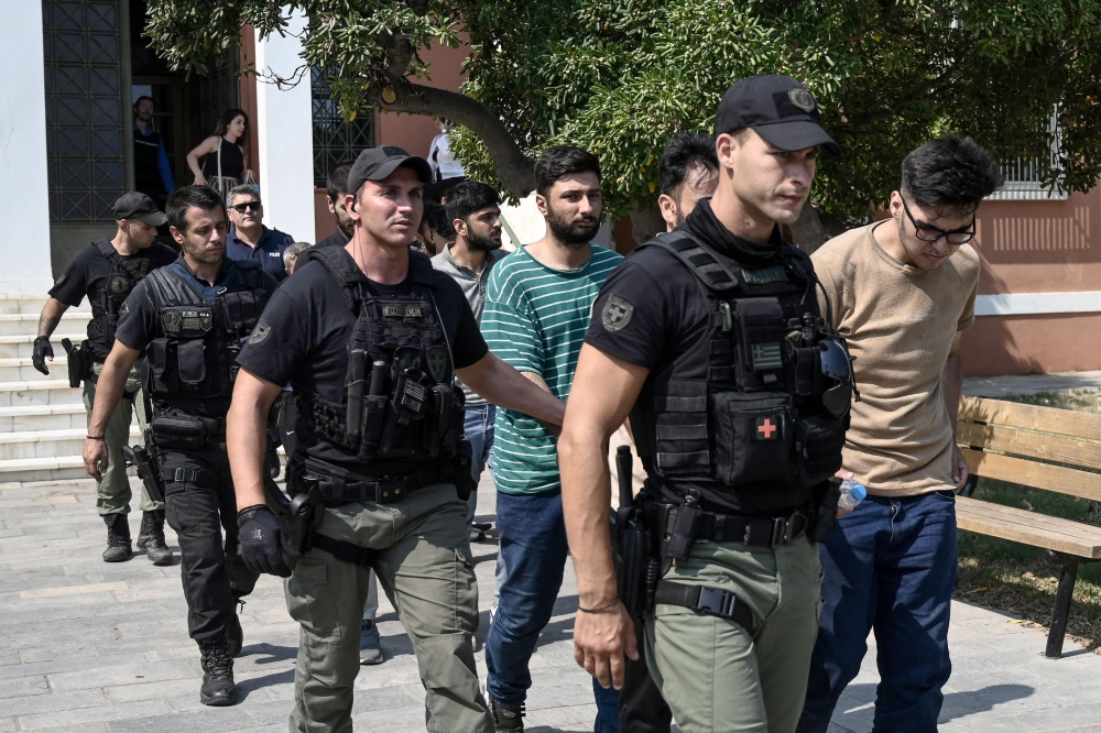 The group of 13 Pakistani and Syrian men charged with illegal entry and attempted arson are escorted at the court house ahead of their hearing in Alexandroupoli on August 25, 2023. (Photo by Sakis MITROLIDIS / AFP)
