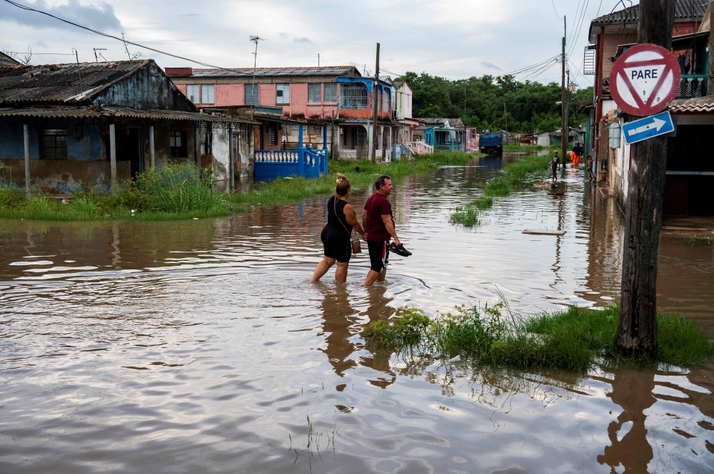 People wade through the water in a flooded area of Batabano, Mayabeque Province, Cuba, on August 28, 2023, as Tropical Storm Idalia approaches the western tip of the island nation. Photo by Yamil LAGE / AFP