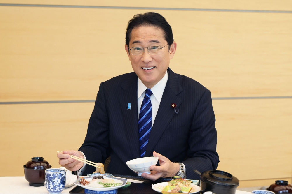 This handout photo taken and received from the Cabinet Public Relations Office via Jiji Press on August 30, 2023 shows Japan's Prime Minister Fumio Kishida posing as he eats seafood from Fukushima prefecture at the prime minister's office in Tokyo. (Photo by Handout / various sources / AFP)