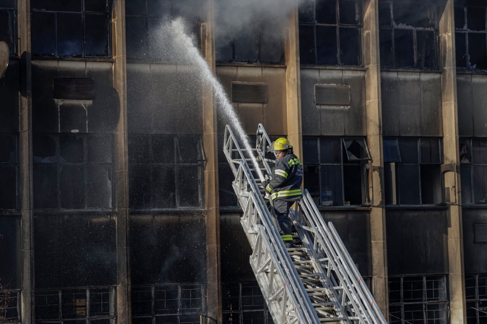Graphic content / A firefighter extinguishes the fire at a building in Johannesburg on August 31, 2023. Photo by Michele Spatari / AFP