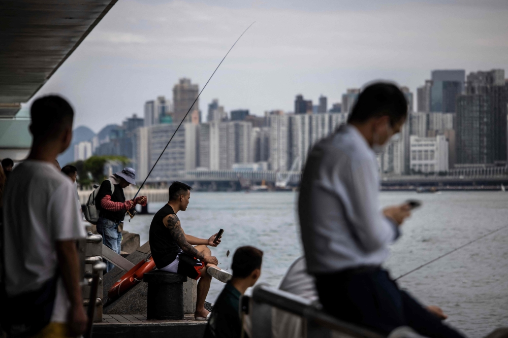 People sit along a promenade next to Victoria harbour in Hong Kong on August 31, 2023, a day before the arrival of Typhoon Saola. (Photo by ISAAC LAWRENCE / AFP)