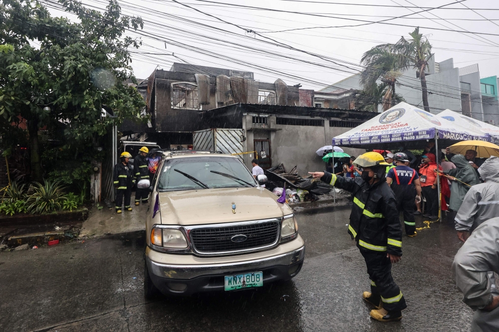 Firemen direct a vehicle after a fire at a house in Quezon City, suburban Manila on August 31, 2023. Photo by AFP