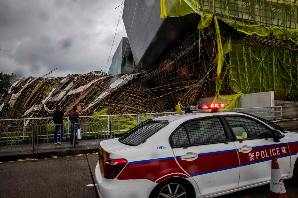 Police drive past bamboo scaffolding that has been brought down by Typhoon Saola at Kowloon Tong in Hong Kong on September 2, 2023. (Photo by Isaac Lawrence / AFP)