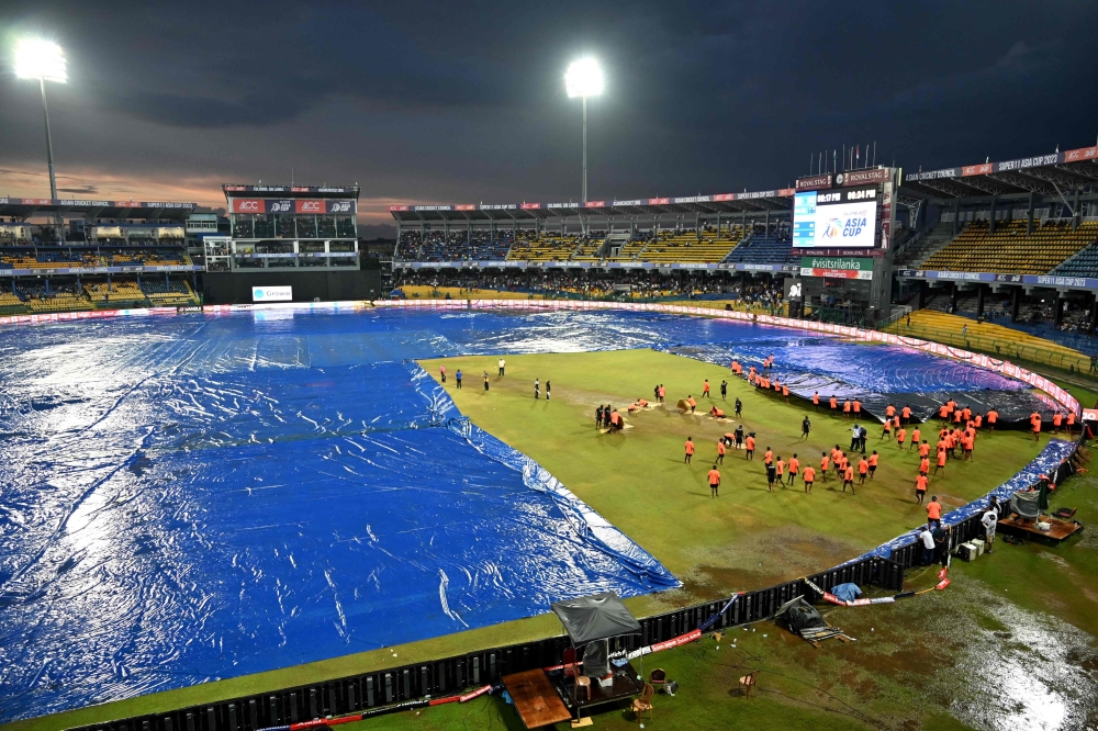 Ground staff cover the pitch after rain stopped play during the Asia Cup 2023 super four one-day international (ODI) cricket match between India and Pakistan at the R. Premadasa Stadium in Colombo on September 10, 2023. (Photo by Farooq Naeem / AFP)