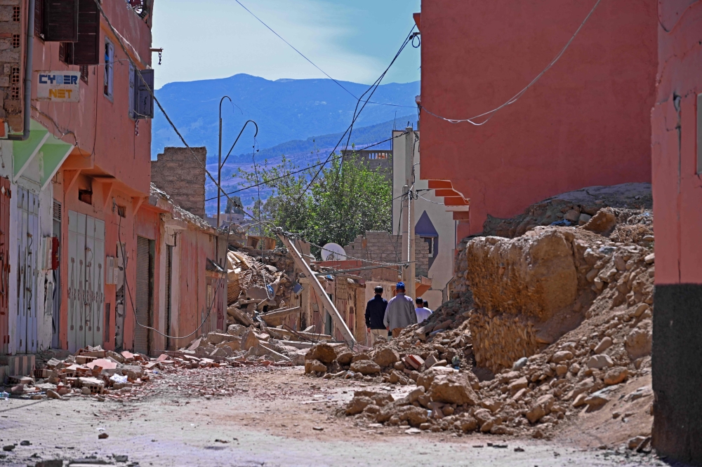 People walk past a destroyed house near Amizmiz in Morocco's worst-hit province of al-Haouz on September 11, 2023. (Photo by AFP)