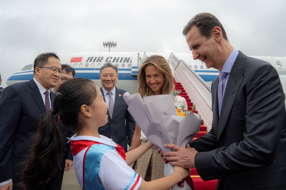 A handout picture released by the official Syrian Arab News Agency (SANA) shows Syria's President Bashar al-Assad (R) and First Lady Asma al-Assad (2-R) being welcomed upon their arrival at the airport in Beijing, on September 21, 2023. (Photo by SANA / AFP) /