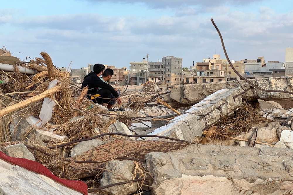 People sit among the rubble in Libya's eastern city of Derna on September 20, 2023, following a deadly flash flood. (Photo by Abu Bakr AL-SOUSSI / AFP)