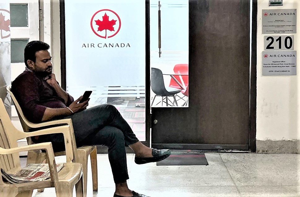A man checks his mobile as he sits outside an Air Canada regional office in New Delhi on September 20, 2023. (Photo by Arun Sankar / AFP)