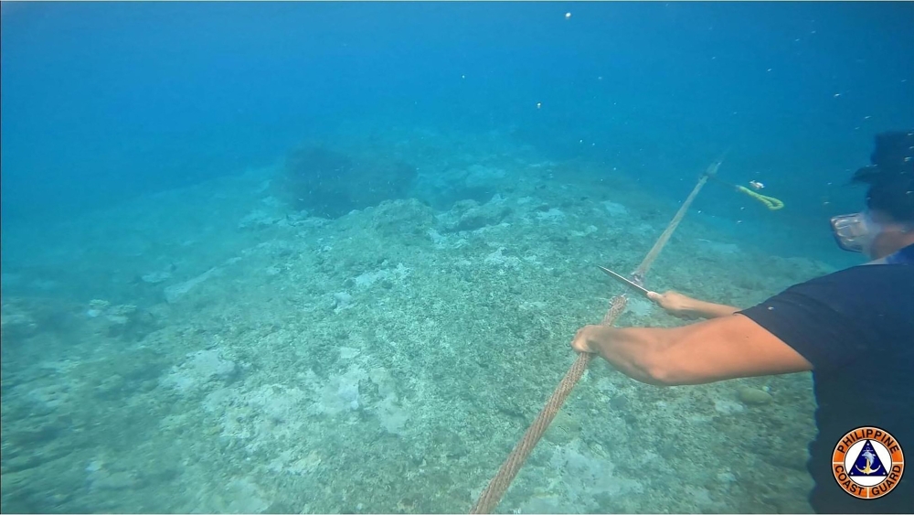 This undated handout photo released on September 25, 2023, by the Philippine Coast Guard (PCG) shows a coast guard personnel cutting a rope attached to a floating barrier blocking the entrance to Scarborough Shoal in the disputed South China Sea. Photo by Philippine Coast Guard (PCG) / AFP