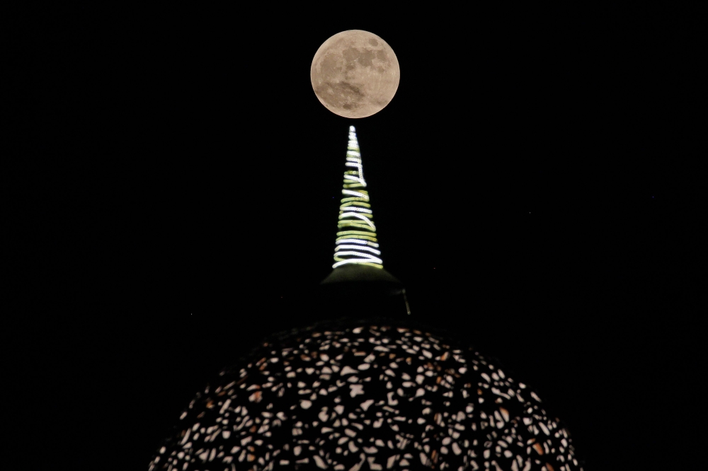 The full moon rises above the dome of a shopping arcade on the outskirts of New Delhi on September 29, 2023. Photo by Vijay MATHUR / AFP