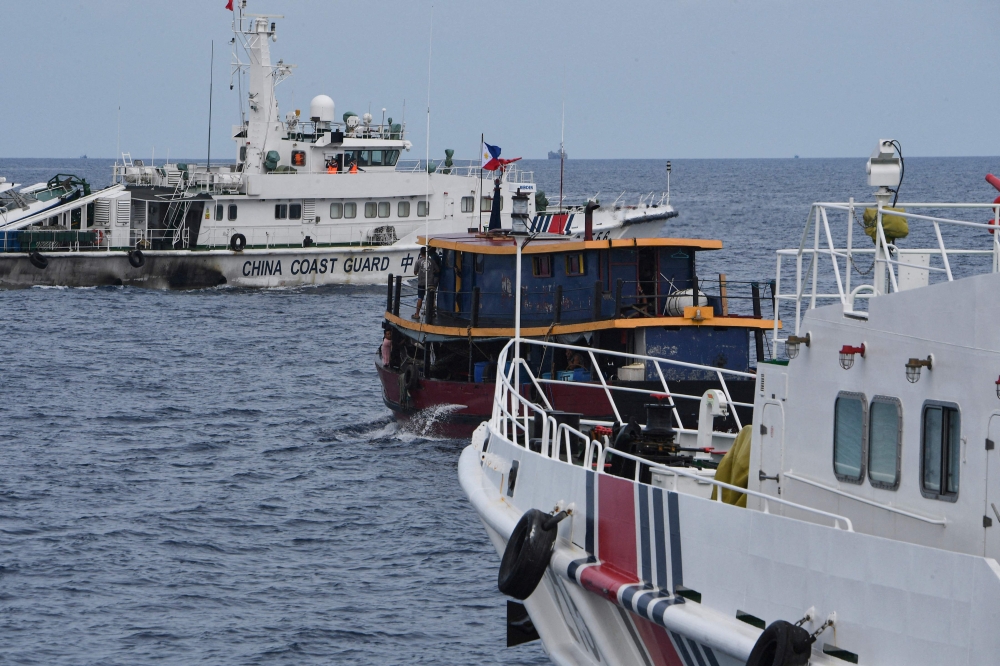 (Files) Chinese coast guard ships (L and R) corral a Philippine civilian boat chartered by the Philippine navy to deliver supplies to Philippine navy ship BRP Sierra Madre in the disputed South China Sea, on August 22, 2023. (Photo by Ted Aljibe / AFP)
