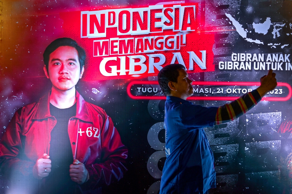 A supporter of Indonesian President Joko Widodo's son and current Surakarta City mayor, Gibran Rakabuming Raka takes a selfie with the latter's poster displayed at an event to raise support for his nomination as the vice presidential candidate ahead of the 2024 presidential elections in Jakarta on October 21, 2023. (Photo by Bay Ismoyo / AFP)
