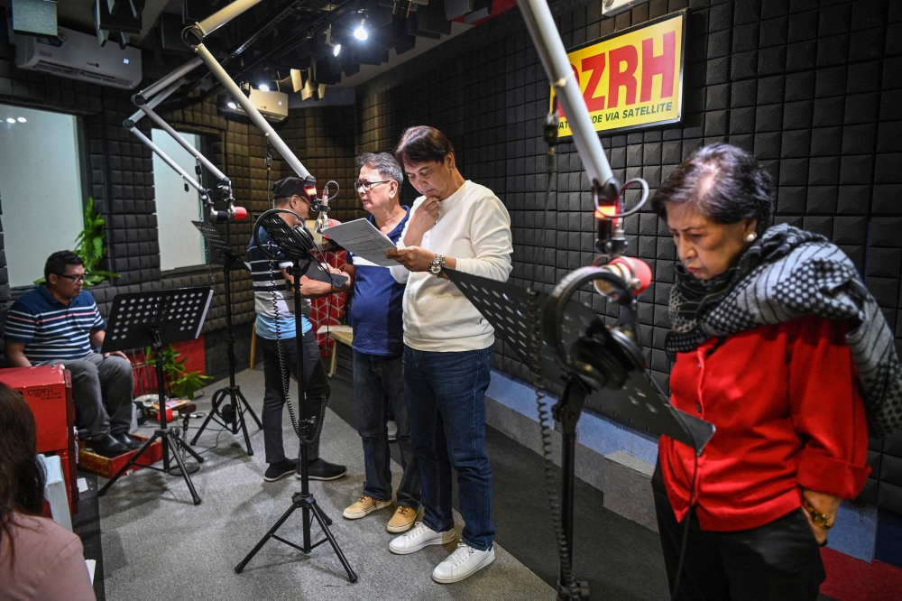 This photo taken on July 17, 2023 shows Phil Cruz (3rd L), his brother Robert (2nd R) and other voice actors recording their part for a radio drama at a studio of a radio station in Manila. (Photo by Ted Aljibe / AFP)