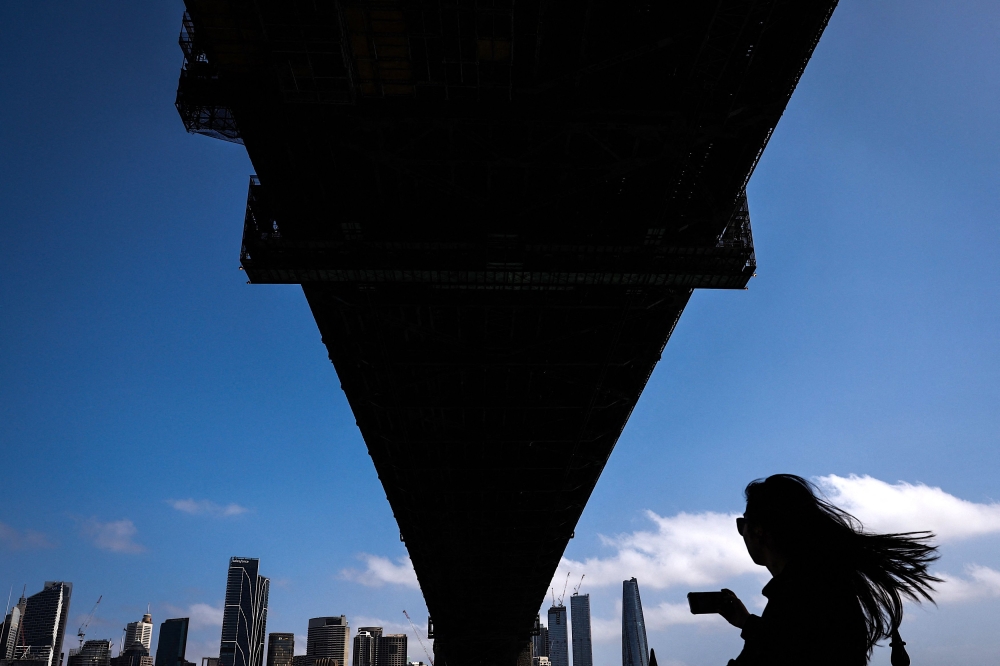 A Chinese tourist takes a photograph with her phone as she walks underneath the Sydney Harbour Bridge on October 25, 2023. Photo by DAVID GRAY / AFP