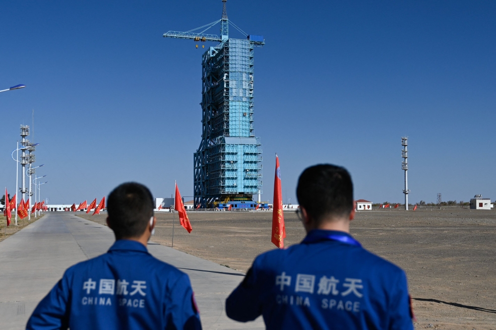 Staff members stand before a Long March-2F carrier rocket, carrying the Shenzhou-17 spacecraft, on the launch pad encased in a shield at the Jiuquan Satellite Launch Centre in the Gobi desert in northwest China on October 25, 2023. Photo by Pedro PARDO / AFP