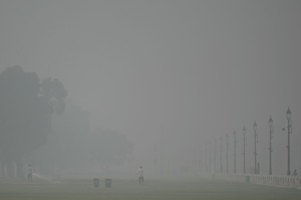 Workers spray water onto a lawn amid heavy smoggy conditions in New Delhi on November 5, 2023. Authorities in the smog-ridden Indian capital New Delhi on November 5 extended an emergency schools closure by a week, with no signs of improvement in the megacity's choking levels of pollution. (Photo by Arun SANKAR / AFP)
