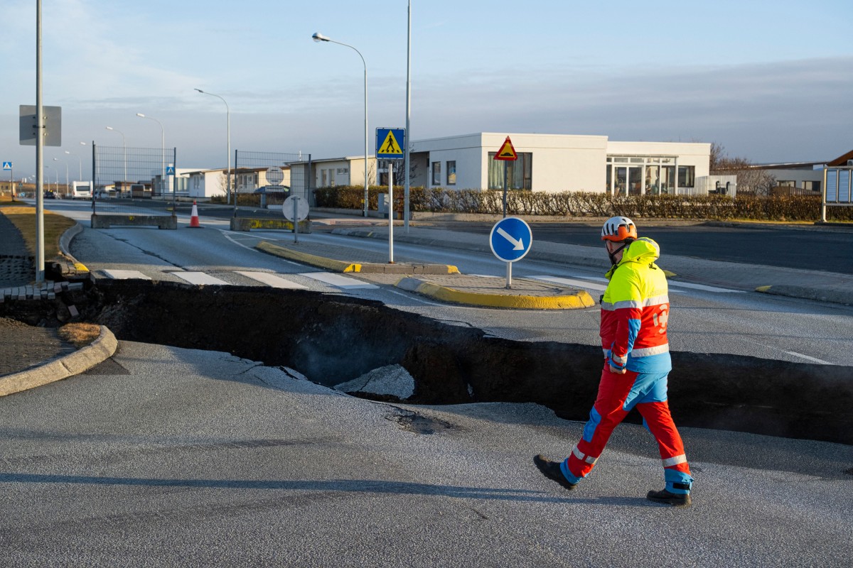 This photo taken on November 13, 2023 shows a member of the emergency services walking near a crack cutting across the main road in Grindavik, southwestern Iceland following earthquakes. Photos by Kjartan TORBJOERNSSON / AFP