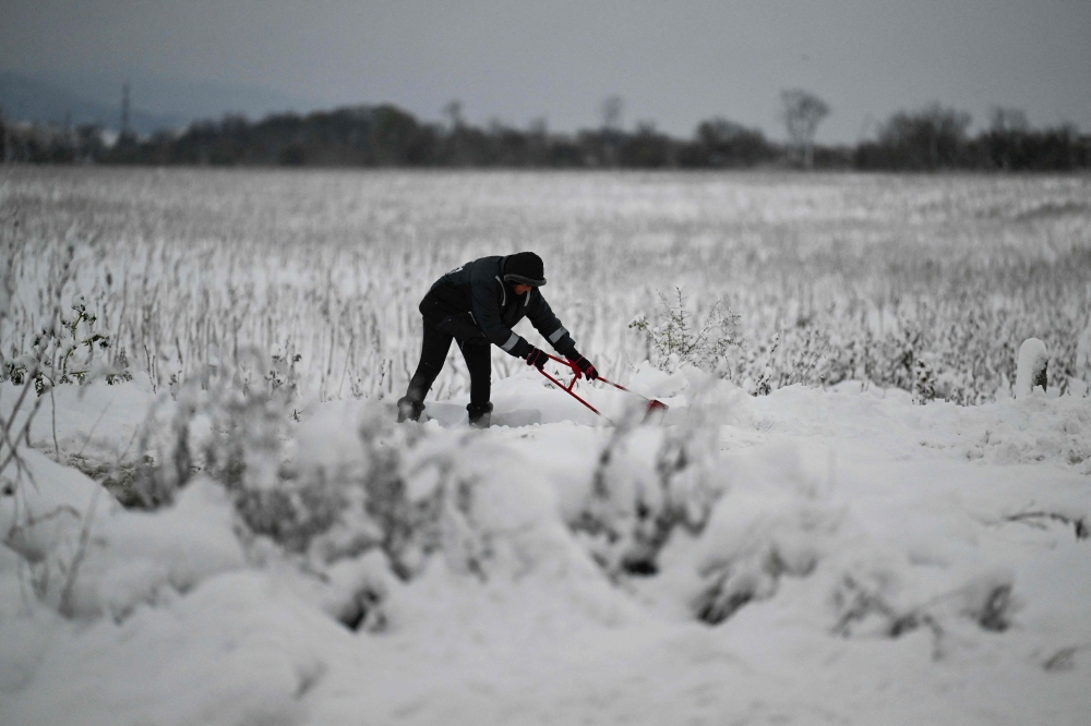 A local resident clears snow from a path after heavy snowfall, on the outskirts of Sofia on November 26, 2023. (Photo by Nikolay DOYCHINOV / AFP)
