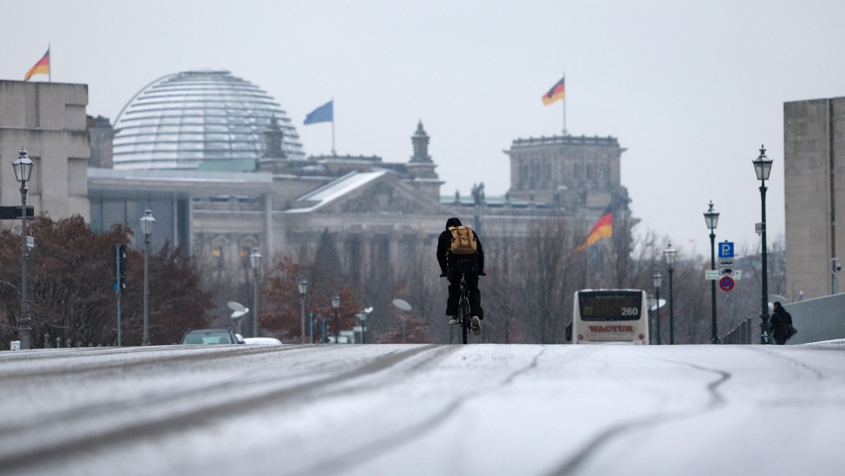 A cyclist drives on a snowy street between the Reichstag building (L) housing the Bundestag (lower house of parliament) and the Chancellery (R) in Berlin's governmental district on November 29, 2023. (Photo by Odd Andersen / AFP)