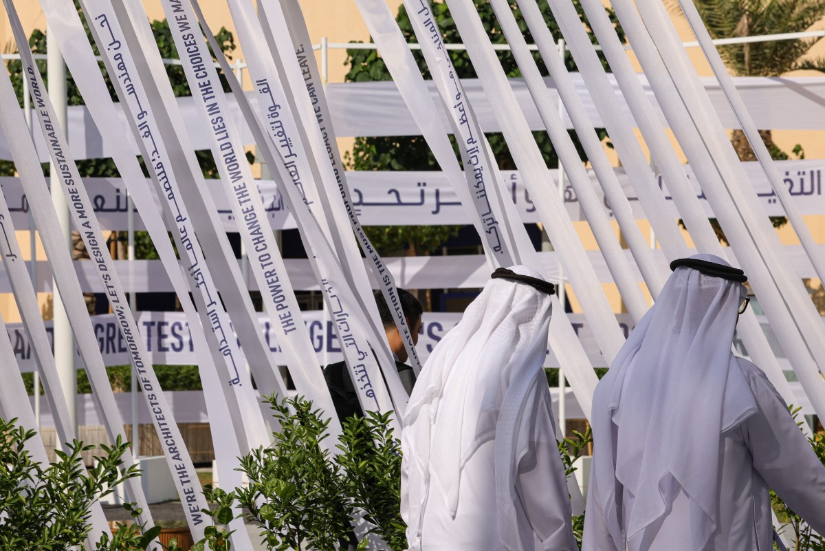 People walk at the venue of the COP28 United Nations climate summit in Dubai on December 6, 2023. (Photo by Giuseppe CACACE / AFP)
