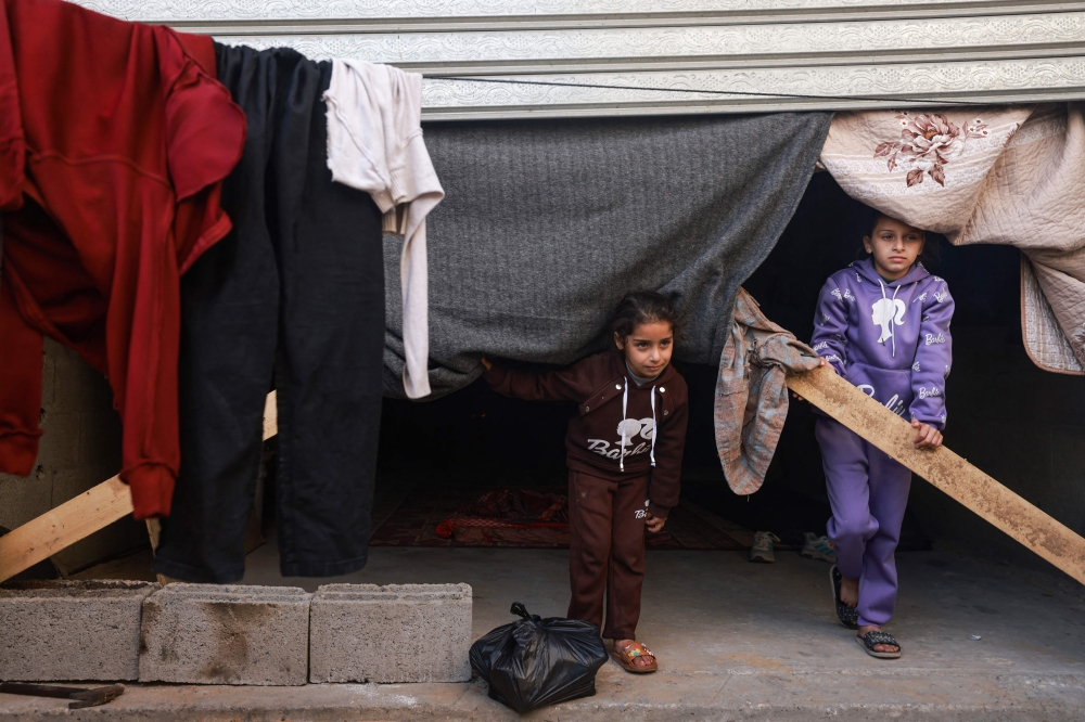 Displaced Palestinian girls stand at the entrance of street shops used as temporary shelter in Rafah in the southern Gaza Strip on December 10, 2023. Photo by MOHAMMED ABED / AFP