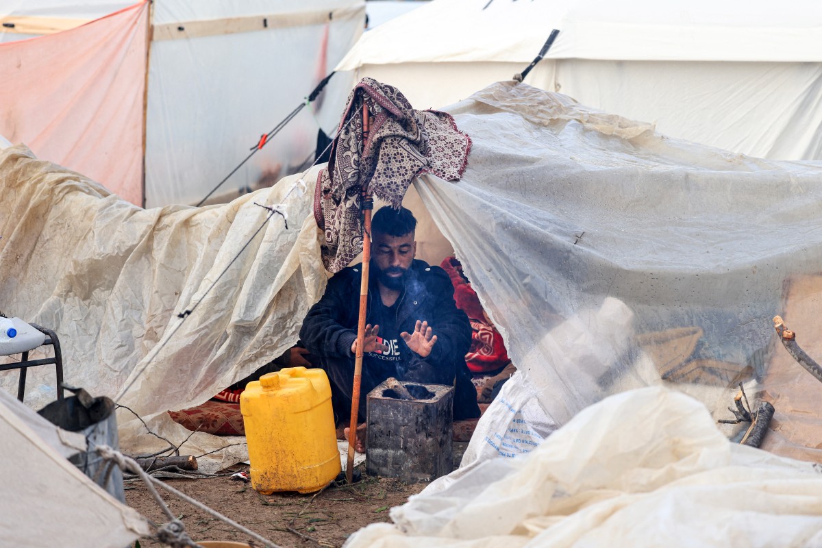 A Palestinian man warms under his makeshift tent at a camp for displaced people in Rafah, in the southern Gaza Strip where most civilians have taken refuge, on December 13, 2023. Photo by MAHMUD HAMS / AFP