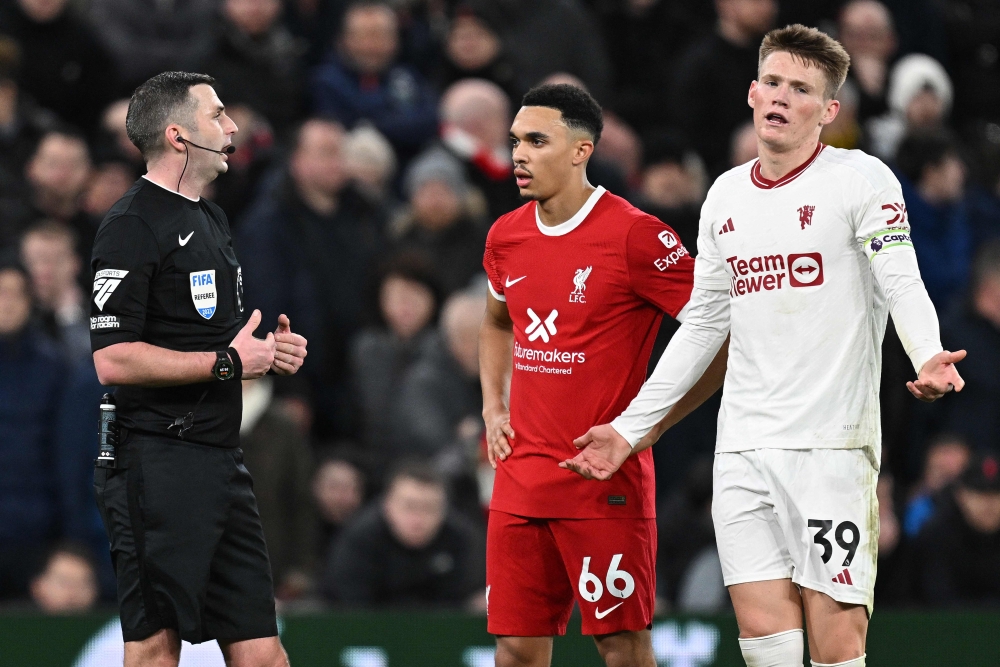 Liverpool's English defender #66 Trent Alexander-Arnold (C) and Manchester United's Scottish midfielder #39 Scott McTominay wait with Referee Michael Oliver for the outcome a VAR review in to a possible Manchester United handball, during the English Premier League football match between Liverpool and Manchester United at Anfield in Liverpool, north west England on December 17, 2023. (Photo by Paul ELLIS / AFP)
