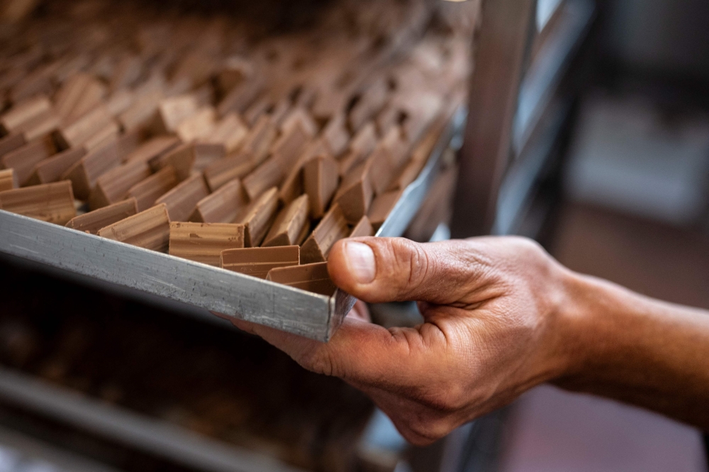 A worker moves a tray of the famous chocolate treat shaped like lingots, the 'Gianduiotto' made with cacao, sugar and hazelnut, on December 12, 2023 in Giaveno near Turin, Northwestern Italy. Photo by MARCO BERTORELLO / AFP
