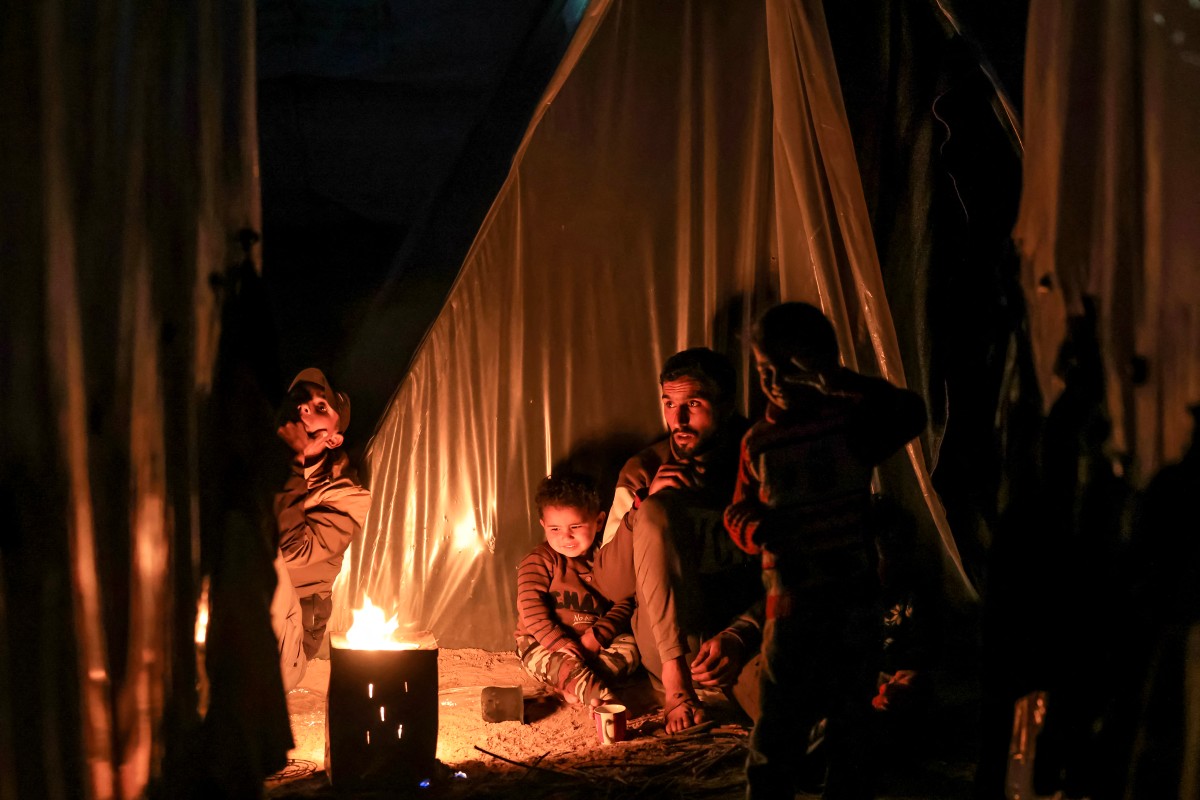 A man sits with children by a fire outside one of the tents housing Palestinians displaced by the conflict in Gaza, in Rafah in the southern Gaza Strip on December 18, 2023. (Photo by Mahmud Hams / AFP)
