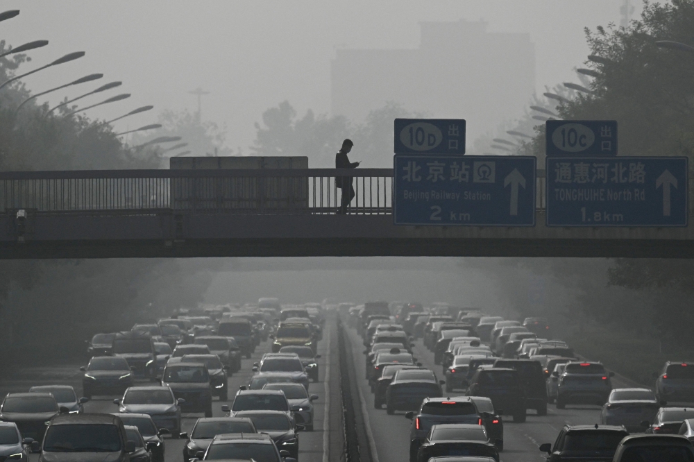 Pedestrians walk on an overpass as traffic snarls amid haze from air pollution in Beijing on November 1, 2023. Photo by Pedro PARDO / AFP