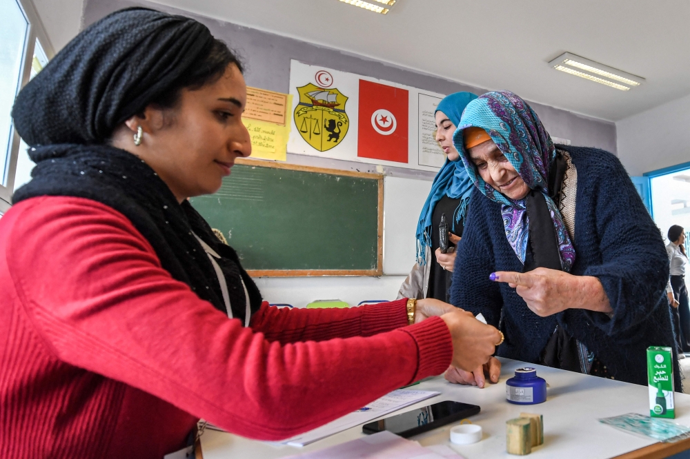 A voter is assisted to dip her finger in ink after voting at a polling station during the 2023 local elections on the outskirts of Tunis on December 24, 2023. (Photo by Fethi Belaid / AFP)