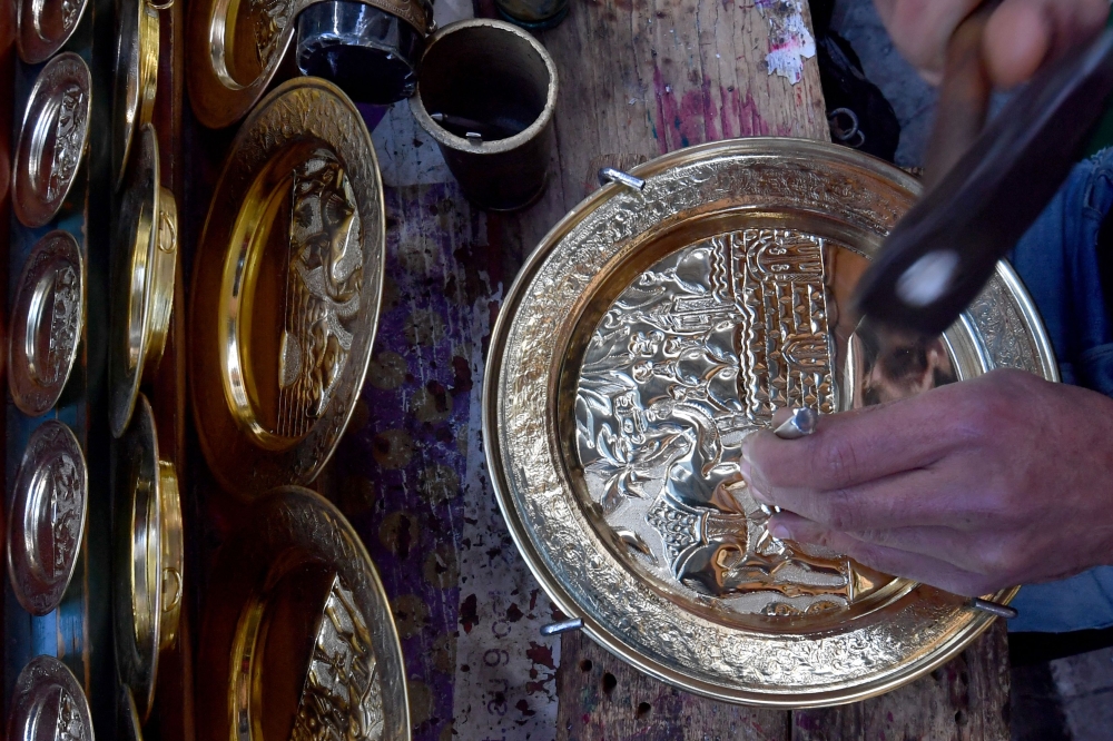 A Tunisian artisan engraves a design onto a copper plate at his shop in the souks of the medina of Tunis on December 7, 2023. (Photo by Fethi Belaid / AFP)