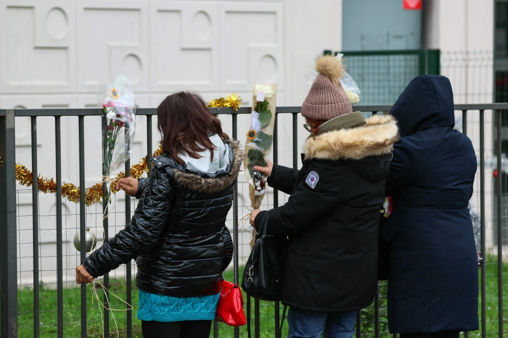 People lay flowers just in front of the ground floor flat where the bodies of a woman and her four children where discovered, in Meaux, eastern Paris, on December 26, 2023. (Photo by Alain Jocard / AFP)