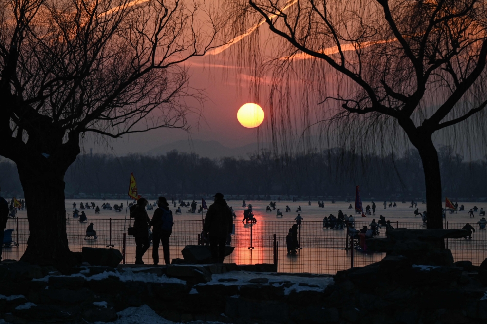People ride sleds on a frozen lake at the Summer Palace during sunset in Beijing on December 28, 2023. (Photo by JADE GAO / AFP)