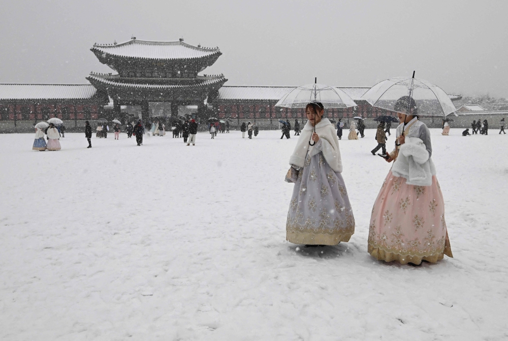 Visitors wearing traditional hanbok dress walk in the snow at Gyeongbokgung palace in central Seoul on December 30, 2023. (Photos by Jung Yeon-je / AFP)