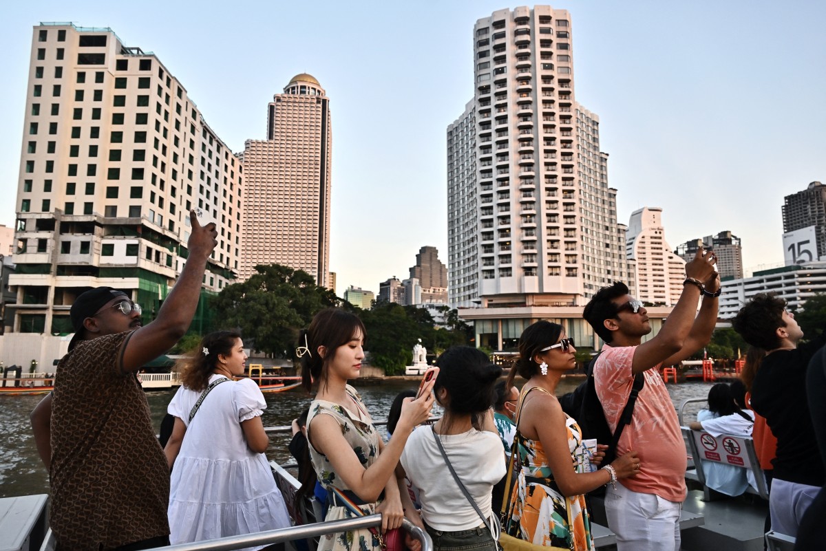 Tourists look at the view from the top deck of a tourist commuter boat on the Chao Praya River in Bangkok on December 27, 2023. (Photo by Lillian SUWANRUMPHA / AFP)
