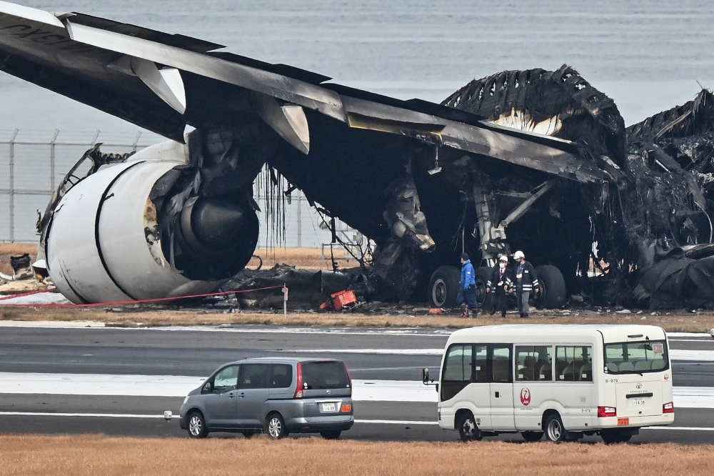 Officials look at the burnt wreckage of a Japan Airlines (JAL) passenger plane on the tarmac at Tokyo International Airport at Haneda in Tokyo on January 3, 2024, the morning after the JAL airliner hit a smaller coast guard plane on the ground. Photo by Richard A. Brooks / AFP