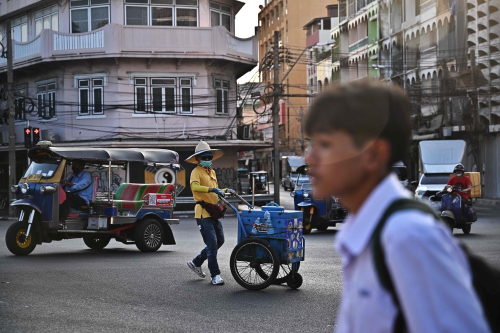 An ice cream vendor crosses an intersection in Bangkok on January 3, 2024. Photo by Lillian SUWANRUMPHA / AFP